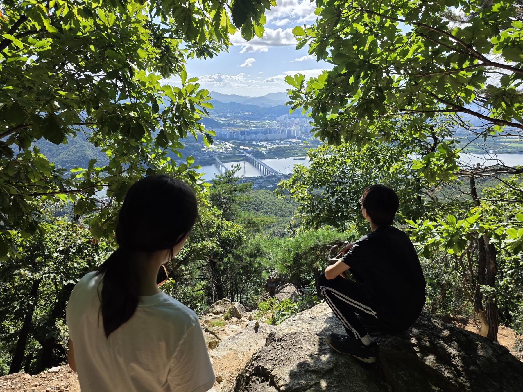 바위에 앉아 산 아래 강과 도시를 내려다보는 두 아이